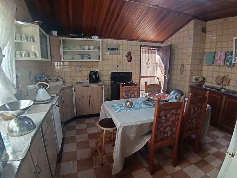 Open-plan kitchen and dining area featuring a vaulted wooden ceiling, tiled finishes, and functional built-in cabinetry with direct access to the exterior.