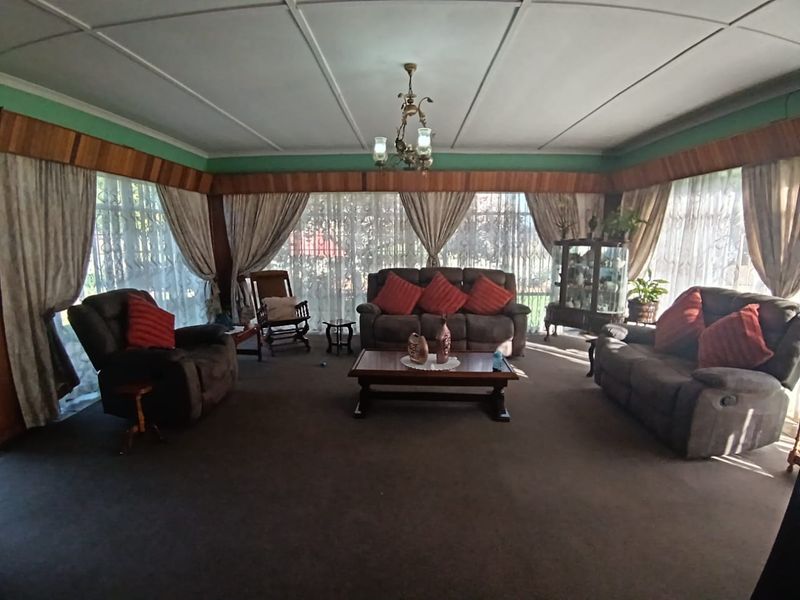 Spacious living room featuring timber wall paneling, decorative ceiling details, and large windows with security bars, offering a traditional layout.