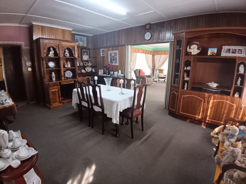 A traditional dining room featuring timber wall paneling and carpet flooring, offering a dated aesthetic with potential for modernization.