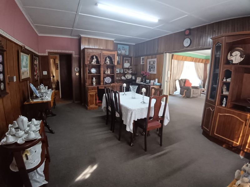 A traditional dining room featuring wood wall paneling, carpet flooring, and a sliding door leading to an adjacent living area.