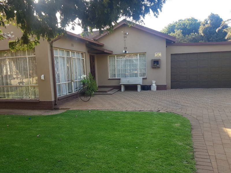 Front elevation of a single-story house featuring a paved driveway, attached double garage, and established front garden.