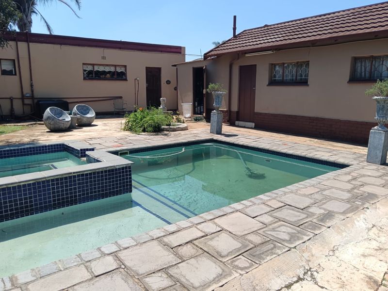 Outdoor pool area featuring a tiled swimming pool with surrounding paving and brick exterior walls of the main house and outbuilding.