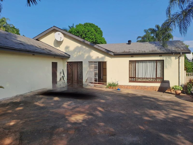 Front elevation of a single-story house featuring a tiled roof, paved driveway, and security gate entrance.