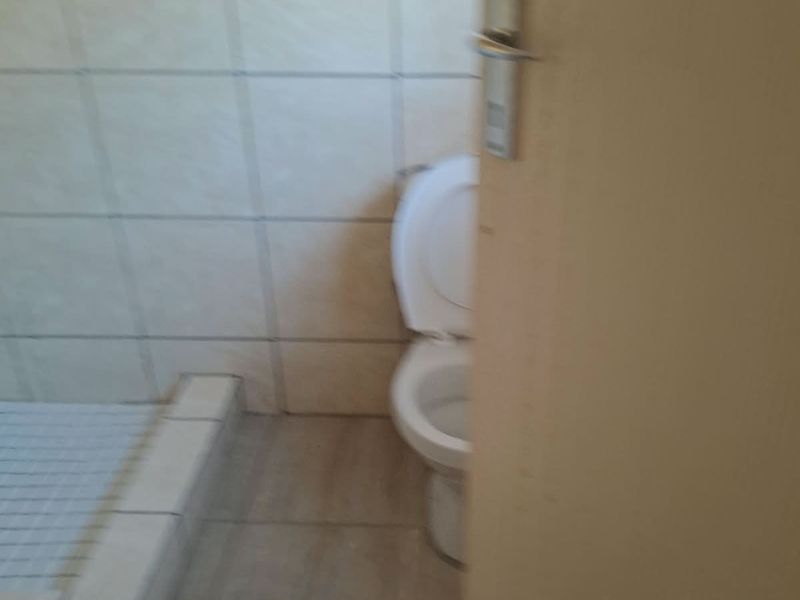 A small bathroom featuring a tiled shower base and a standard toilet, viewed through a partially open doorway.