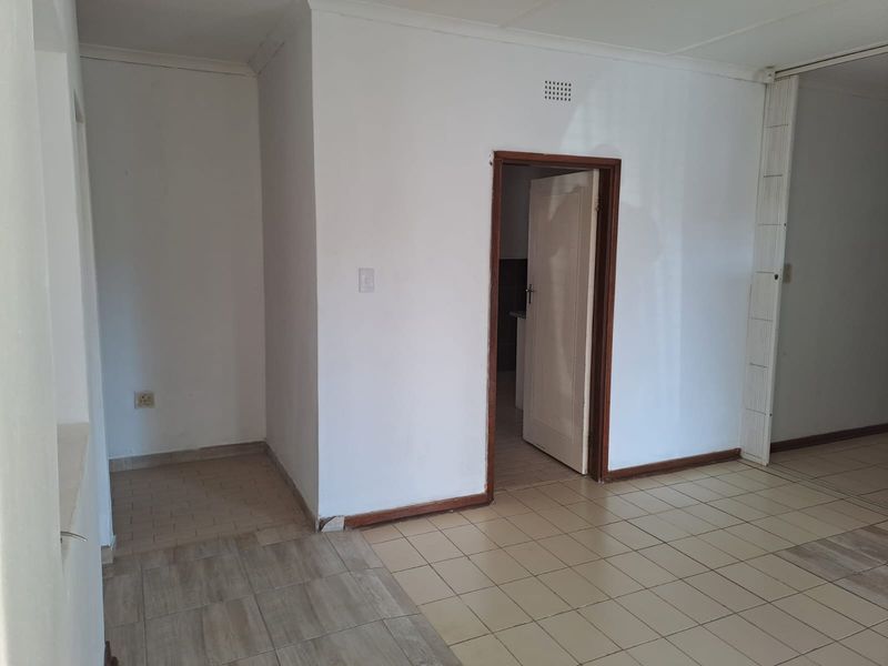 An empty living area featuring tiled flooring and a doorway leading to an adjacent room, presenting a blank canvas for renovation.