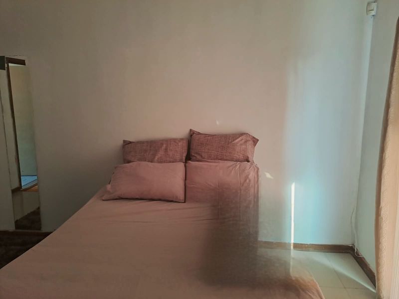 A bedroom interior featuring plain walls and tiled flooring, currently furnished with a bed.