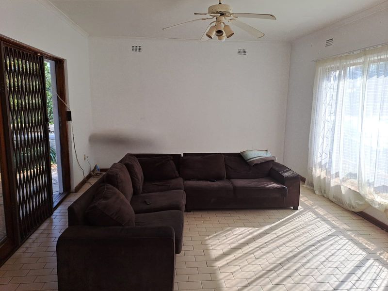 A living room featuring tiled flooring, a ceiling fan, and access to an outdoor area through a security gate.