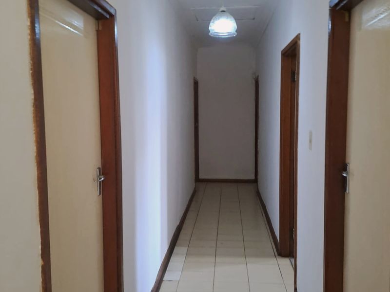 A narrow interior hallway featuring tiled flooring and wooden door frames leading to multiple rooms.