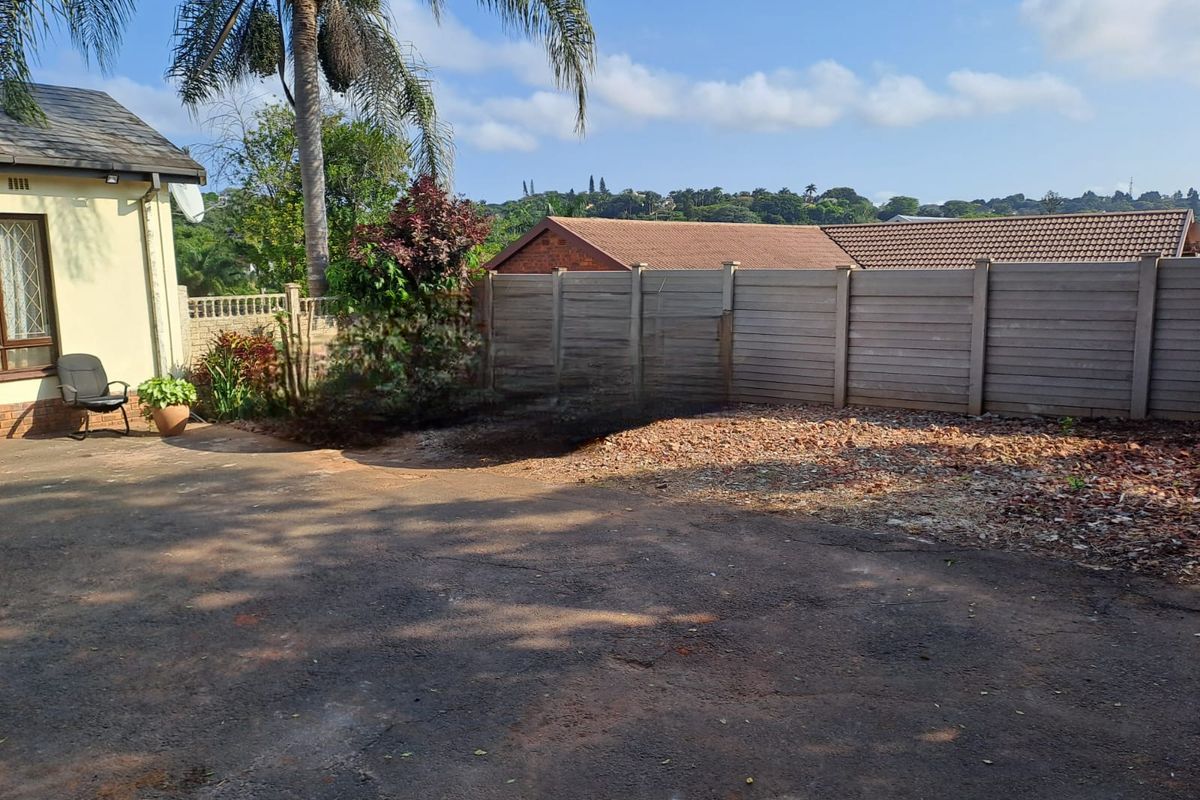 Rear exterior area featuring an asphalt driveway, precast concrete boundary wall, and established garden space with mature palm tree.