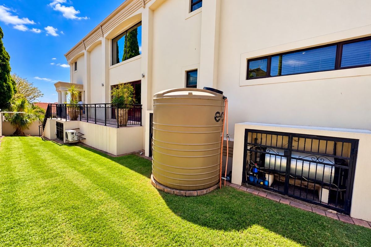 Rear exterior view of the property featuring a well-maintained lawn, a raised patio with wrought iron railings, and a large water storage tank.