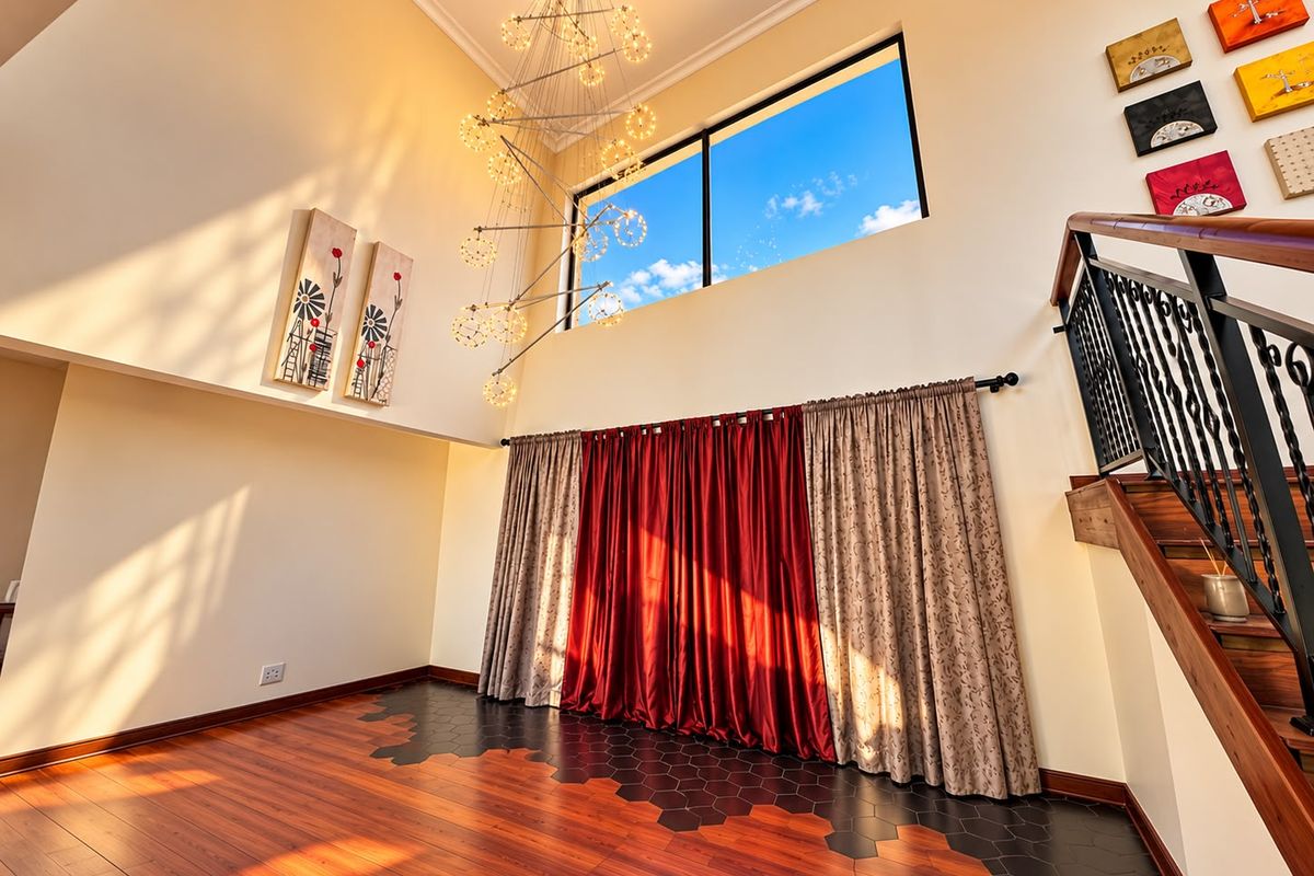 Spacious double-volume living area featuring a striking chandelier, large clerestory window, and unique mixed-material flooring with a timber staircase and wrought iron balustrade.
