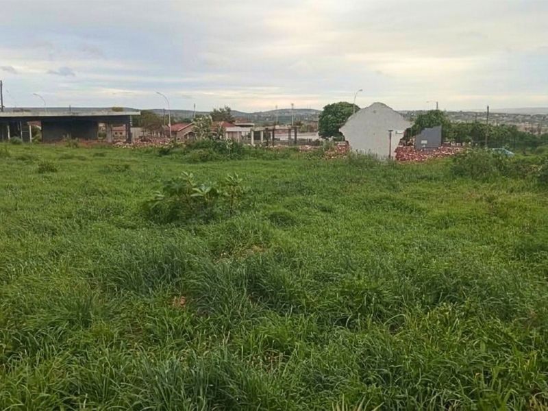 A view of a vacant residential plot featuring overgrown grass and surrounding neighborhood infrastructure.