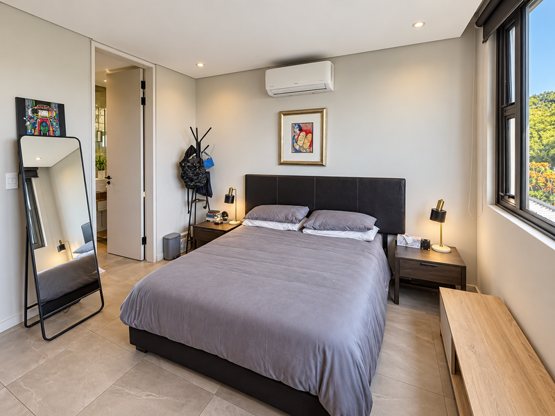 A well-maintained bedroom featuring modern tiled flooring, a split-system air conditioner, and large windows allowing for natural light.
