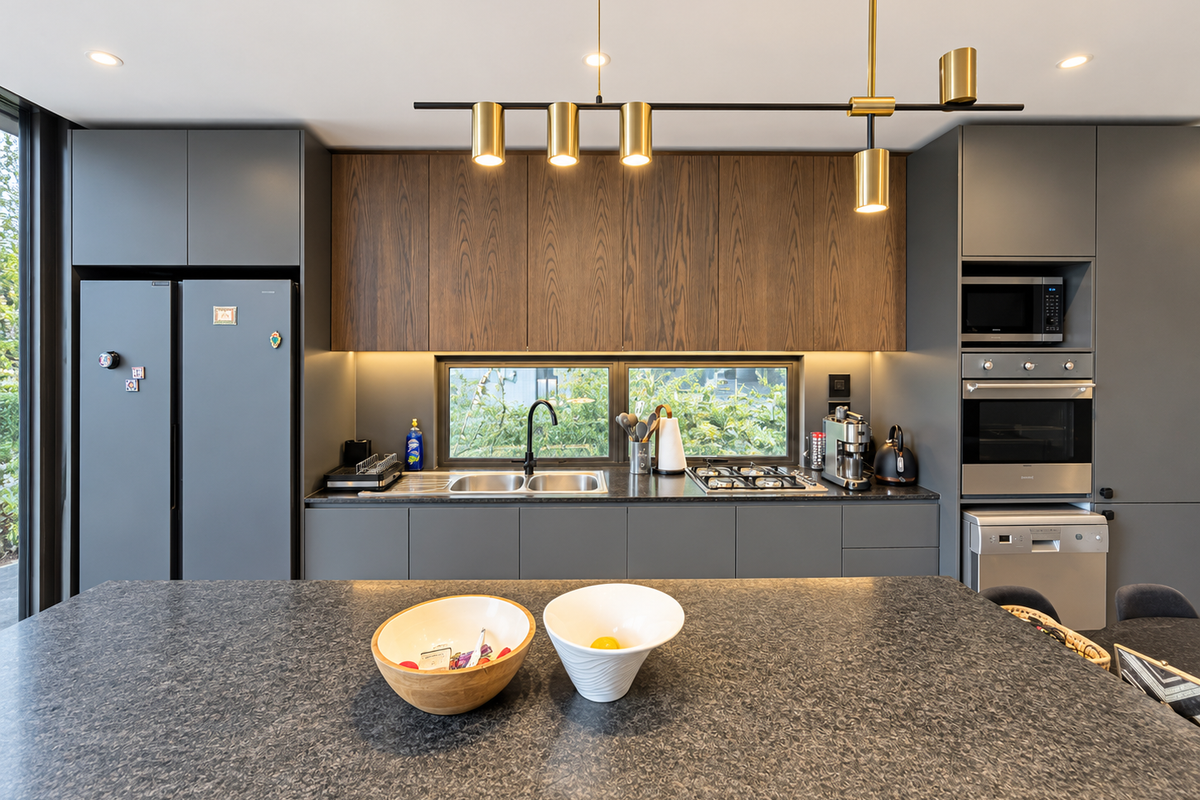 Modern kitchen featuring dark grey cabinetry, wood-grain upper cabinets, stone countertops, a central island, and high-end built-in appliances with integrated lighting.