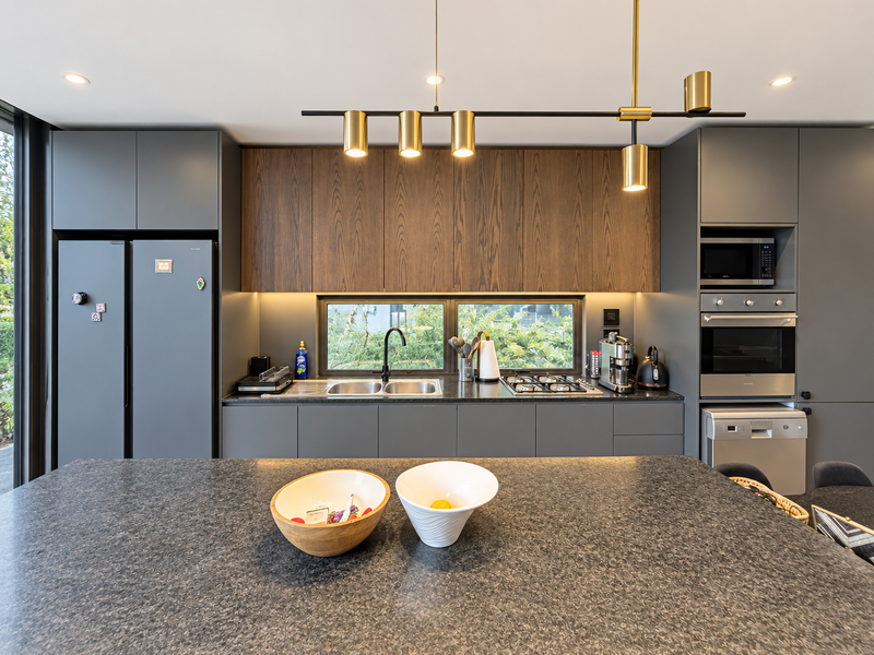 Modern kitchen featuring dark grey cabinetry, wood-grain upper cabinets, stone countertops, a central island, and high-end built-in appliances with integrated lighting.