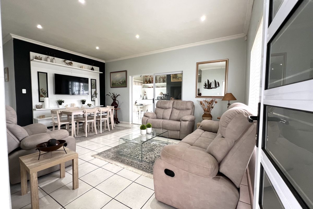 Spacious living room featuring tiled flooring, recessed downlights, and a custom built-in shelving unit, with seamless access to an adjacent dining area.