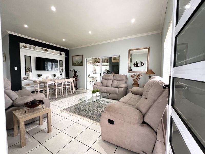Spacious living room featuring tiled flooring, recessed downlights, and a custom built-in shelving unit, with seamless access to an adjacent dining area.