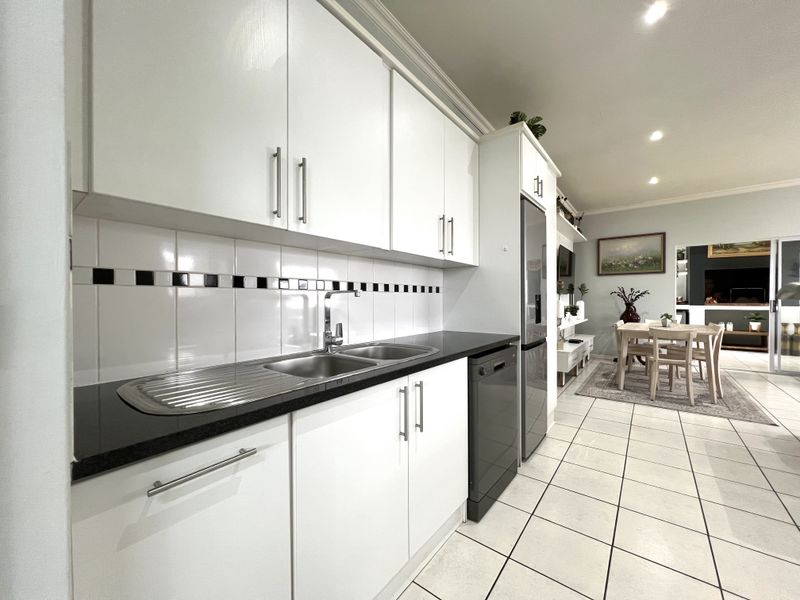Open plan kitchen featuring white cabinetry, black granite countertops, and a tiled backsplash, flowing seamlessly into the adjacent dining and living area.
