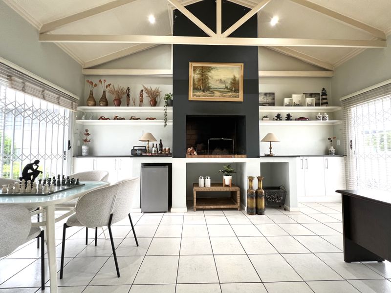 A spacious, covered patio area featuring a vaulted ceiling with exposed timber trusses, a central built-in fireplace, and extensive built-in cabinetry.