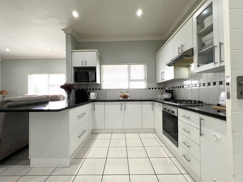 Modern kitchen featuring white cabinetry, black granite countertops, gas hob, built-in oven, extractor fan, and tiled flooring, seamlessly flowing into the adjacent living area.