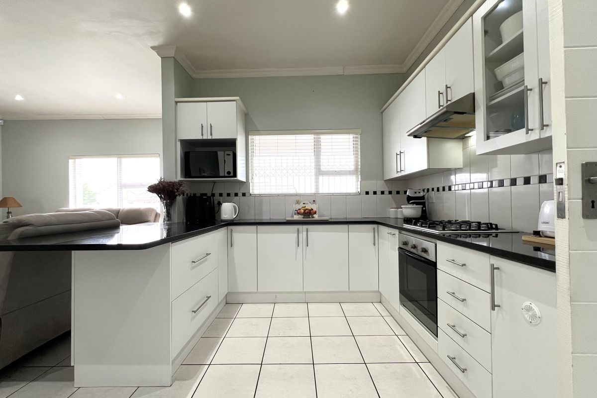 Modern kitchen featuring white cabinetry, black granite countertops, gas hob, built-in oven, extractor fan, and tiled flooring, seamlessly flowing into the adjacent living area.