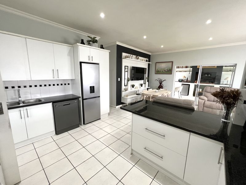 Modern open-plan kitchen and living area featuring white cabinetry, granite countertops, a central island, and tiled flooring throughout.