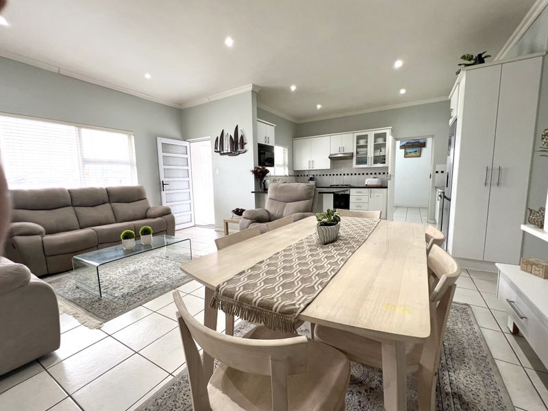 An open-plan living, dining, and kitchen area featuring tiled flooring, recessed lighting, and a functional kitchen with built-in cabinetry and appliances.