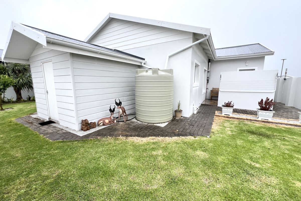 Rear exterior view of the property featuring a paved walkway, white siding, and a water storage tank set against a well-maintained lawn.