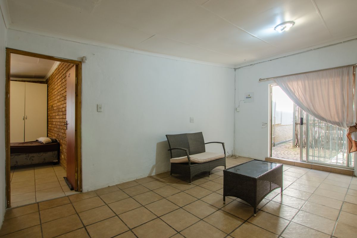 A simple living area featuring tiled flooring and a sliding glass door leading to an outdoor space, with an adjacent bedroom visible.