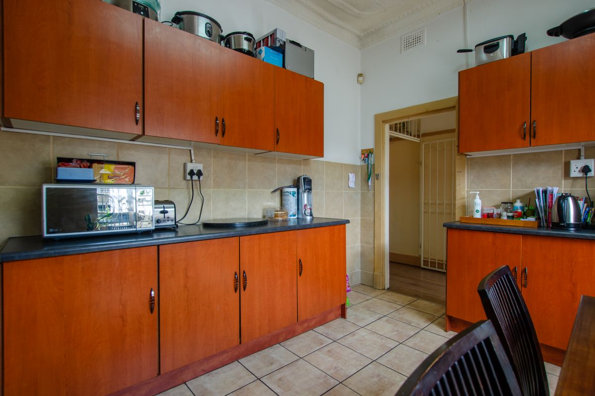 A functional kitchen featuring wood-look laminate cabinetry, tiled backsplash, and durable floor tiles, offering a practical layout with ample storage space.