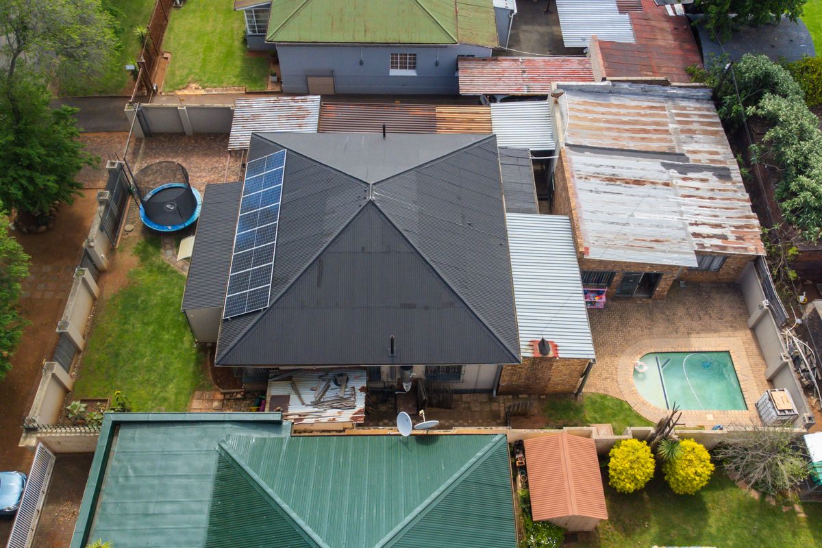 Aerial view of the property showing the main house with solar panels, a swimming pool, paved patio areas, and surrounding garden space.