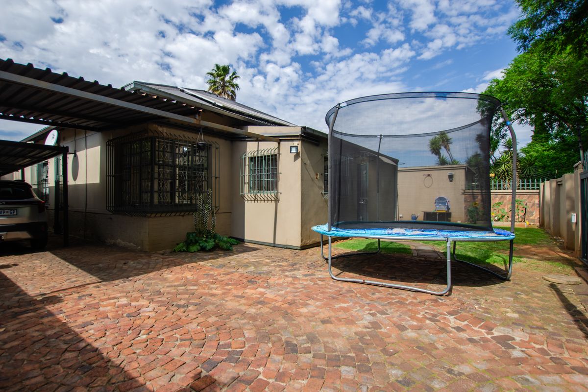 Rear exterior view featuring a brick paved courtyard, carport, and secure boundary walling.