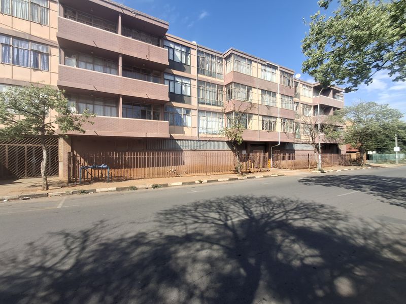 Street-level view of a multi-story apartment building featuring a brick facade, private balconies, and secure perimeter fencing.