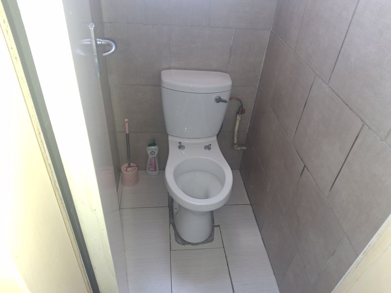 A small bathroom featuring a standard toilet with tiled walls and flooring, showing signs of wear and dated finishes.