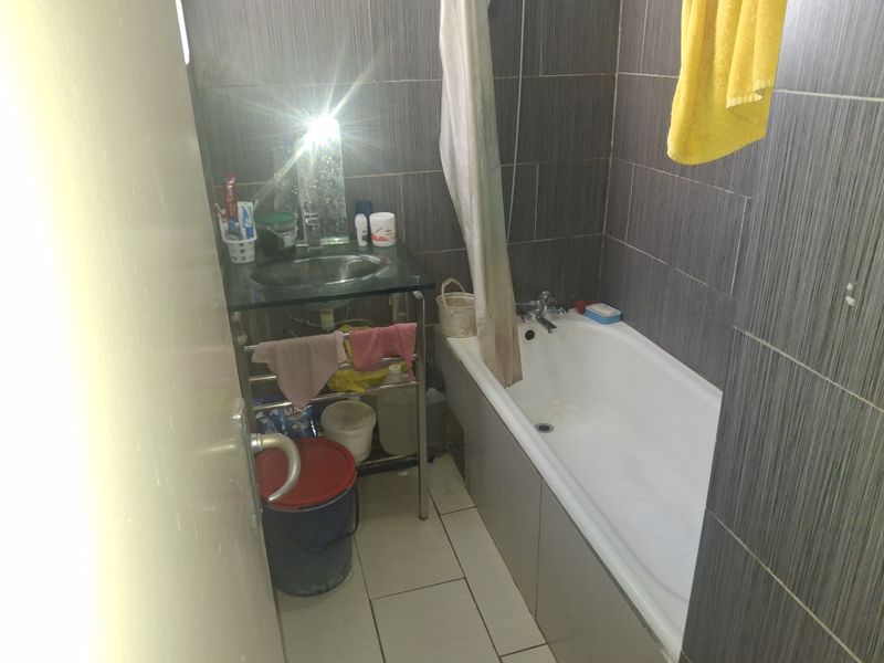 A compact bathroom featuring a bathtub, basin, and dark grey wall tiling. The space requires maintenance and cosmetic updates to improve its overall condition.