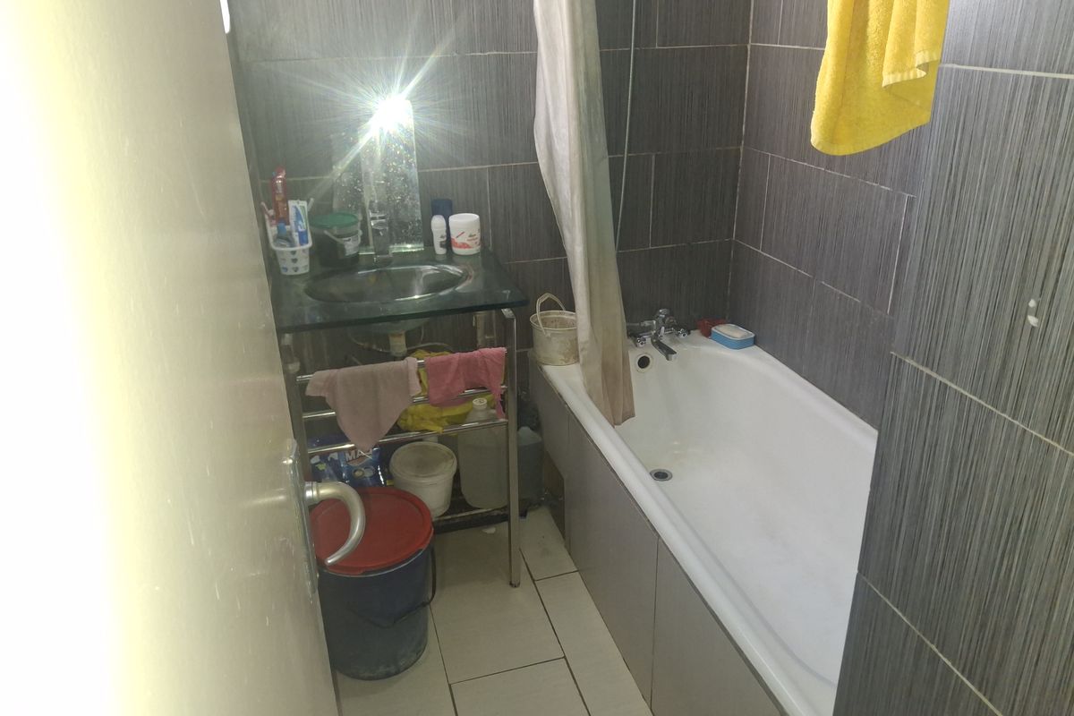 A compact bathroom featuring a bathtub, basin, and dark grey wall tiling. The space requires maintenance and cosmetic updates to improve its overall condition.