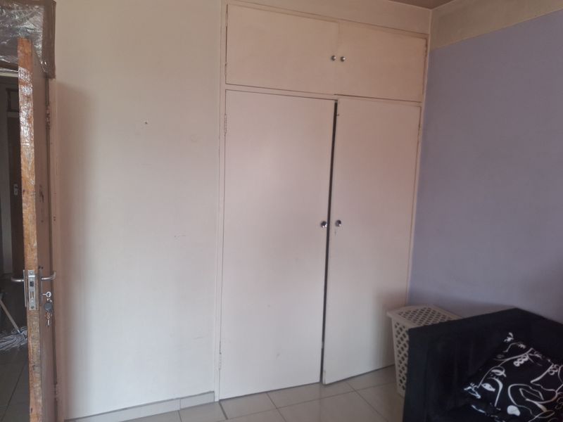A bedroom featuring built-in cupboards with overhead storage and tiled flooring, requiring minor cosmetic updates to improve the overall aesthetic.