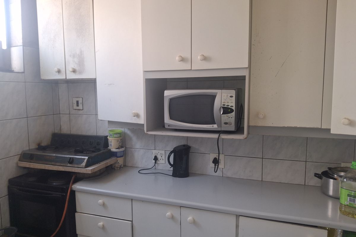 A dated kitchen featuring white cabinetry, tiled backsplash, and a built-in microwave shelf, requiring cosmetic updates to improve its overall condition and appeal.