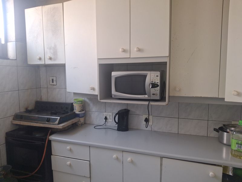 A dated kitchen featuring white cabinetry, tiled backsplash, and a built-in microwave shelf, requiring cosmetic updates to improve its overall condition and appeal.