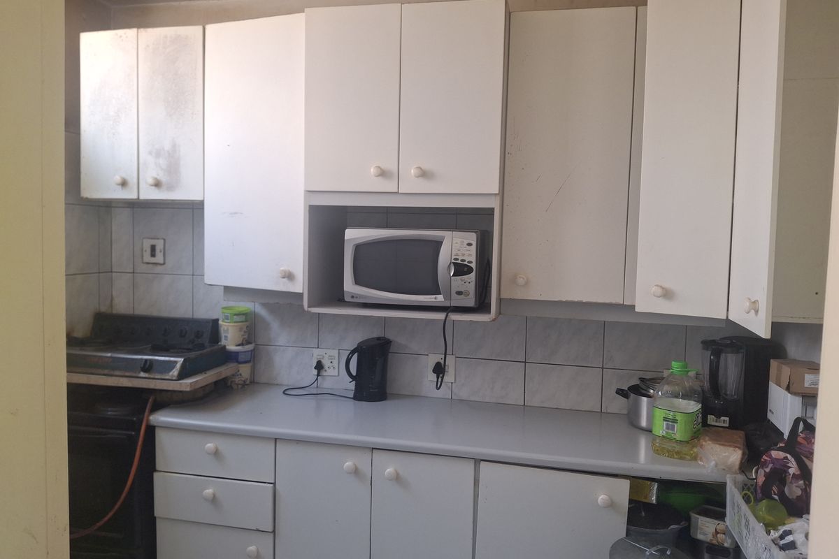 A compact kitchen featuring white cabinetry, tiled backsplash, and a laminate countertop, currently showing signs of wear and requiring cosmetic updates.