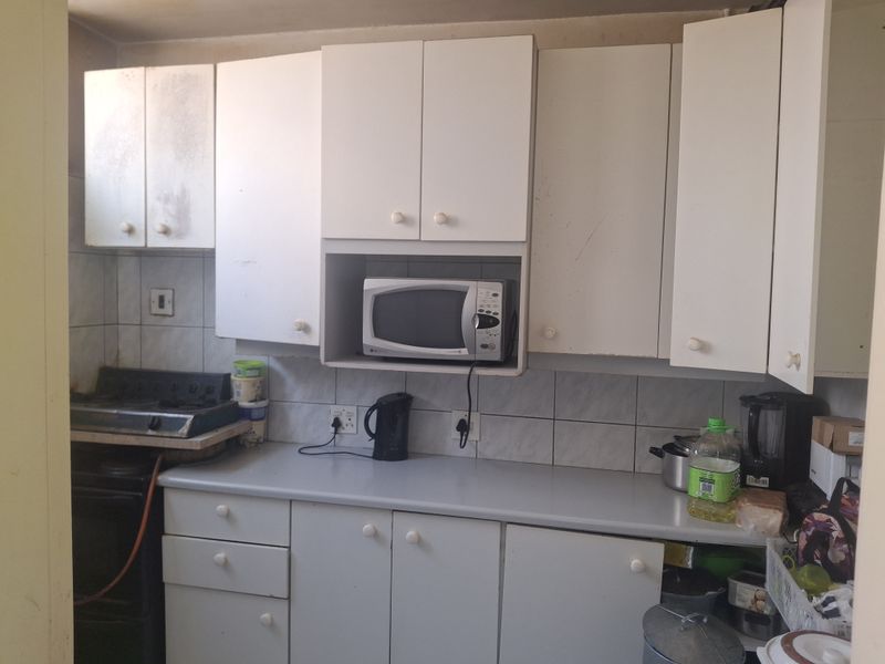 A compact kitchen featuring white cabinetry, tiled backsplash, and a laminate countertop, currently showing signs of wear and requiring cosmetic updates.