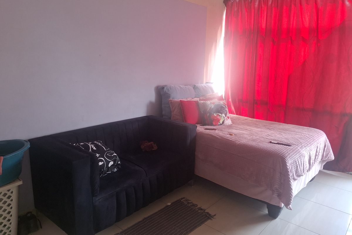 A bedroom featuring tiled flooring and a window covered by red curtains.
