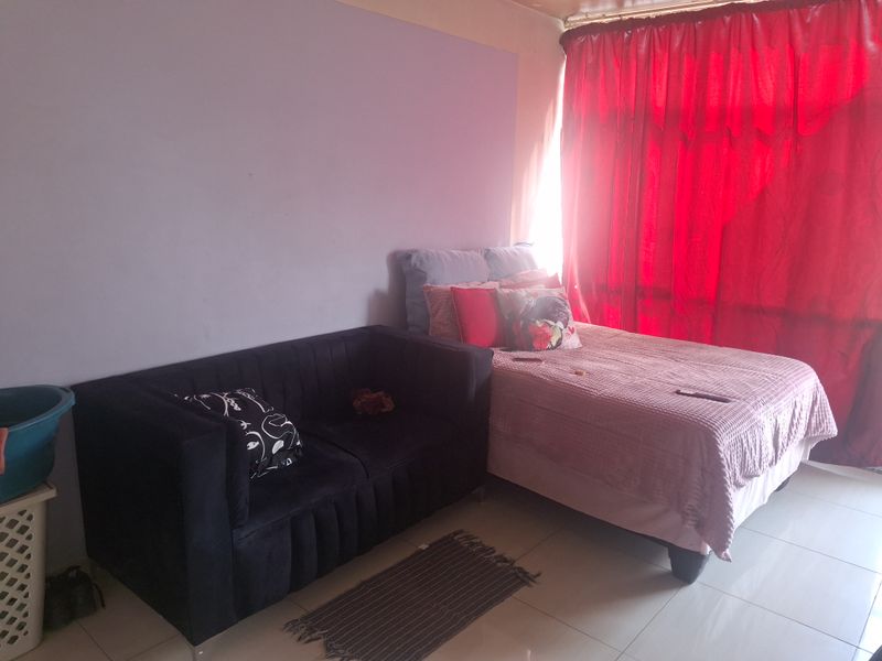 A bedroom featuring tiled flooring and a window covered by red curtains.