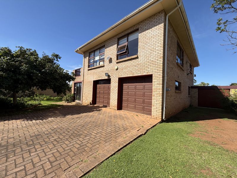 A double-storey face brick house featuring a double garage, paved driveway, and established garden surroundings.