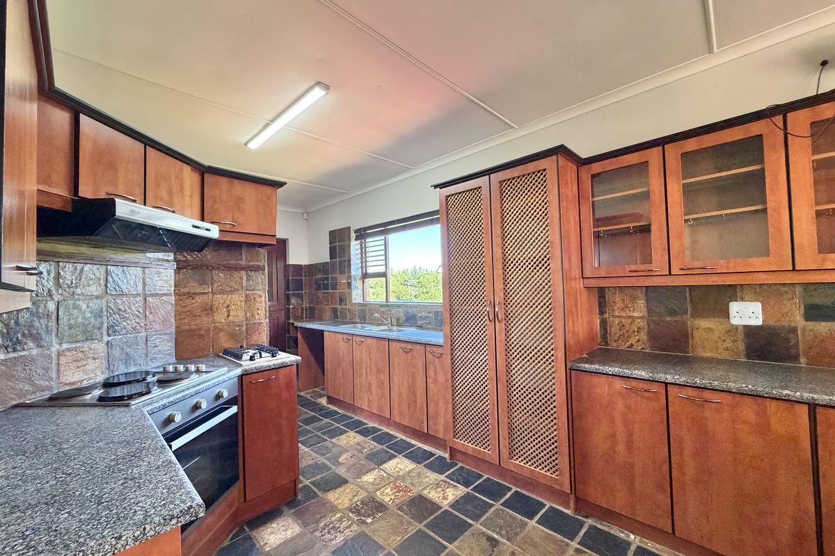 A functional kitchen featuring wooden cabinetry, granite countertops, built-in oven, gas hob, and stone tile finishes throughout.