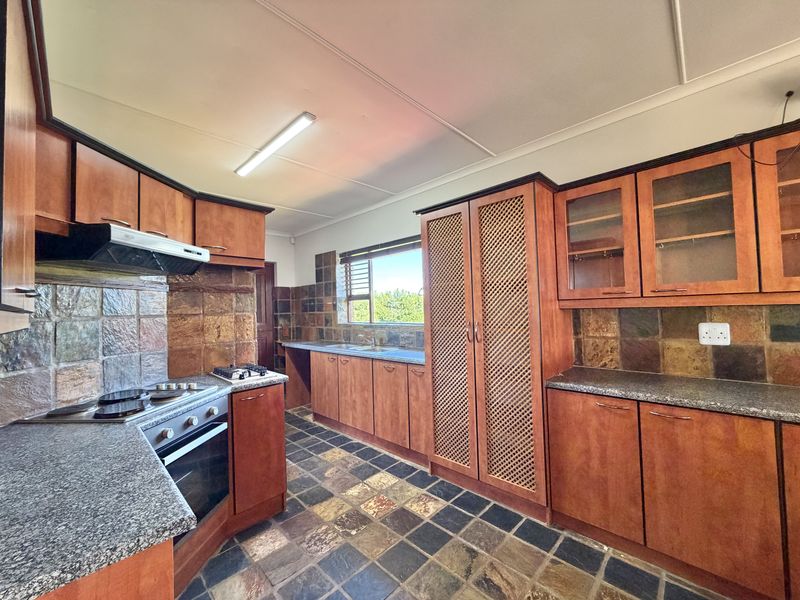 A functional kitchen featuring wooden cabinetry, granite countertops, built-in oven, gas hob, and stone tile finishes throughout.