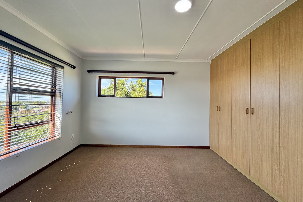 A bright, empty bedroom featuring neutral walls, carpeted flooring, and extensive built-in wooden cupboards with natural light from multiple windows.
