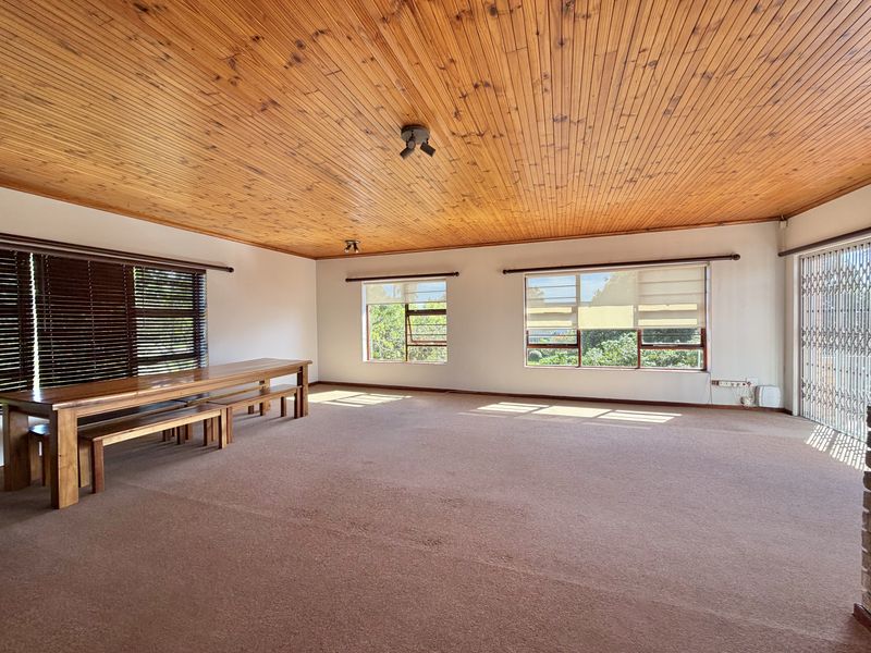 Spacious living area featuring a timber tongue and groove ceiling, large windows with natural light, and carpeted flooring.