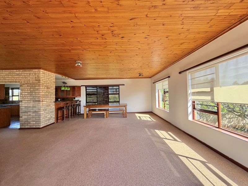 Spacious open-plan living and dining area featuring a warm timber ceiling, exposed brick accents, and large windows that provide ample natural light.