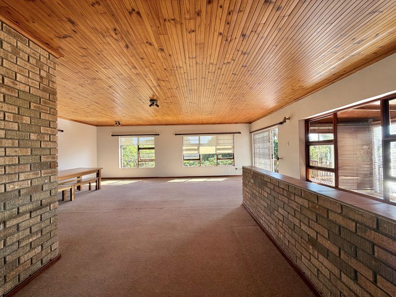 Spacious living area featuring a warm timber tongue and groove ceiling, exposed brick accents, and large windows providing ample natural light.